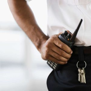 Close-up of a hospital security guard's hand holding a walkie-talkie, with a key ring attached to their belt.