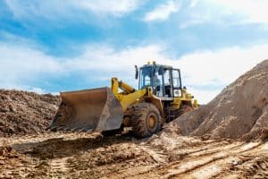 A yellow bulldozer moves a large pile of dirt at a construction site under a clear blue sky, while construction site security ensures the area remains safe and secure.