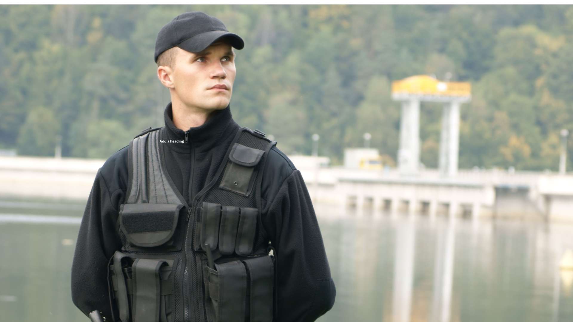 A uniformed security guard, wearing a cap and tactical vest, stands by a body of water with a bridge and greenery in the background.