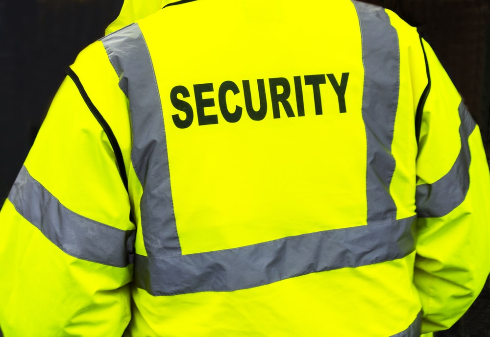 Close-up of the back of a person wearing a bright yellow jacket with reflective stripes, labeled "SECURITY" in bold black letters.