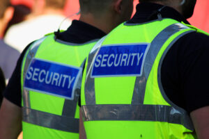 Two individuals in bright yellow vests labeled "SECURITY" stand in an outdoor setting, their presence highlighting the vital role of Special Event Security Oakland County in ensuring safety. The photograph captures them from behind, emphasizing their commitment to safeguarding the area.